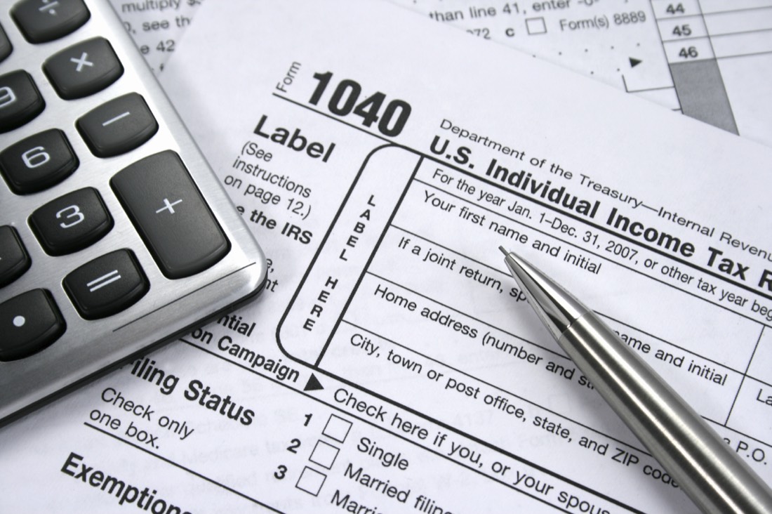 A 1040 personal income tax form with a calculator and pen on a desk